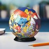 Na zdjęciu znajduje się kuliste puzzle 3D z motywem postaci z serii Pokemon, umieszczone na czarnej podstawce. W tle widać rozmyte elementy, a na pierwszym planie leży ołówek.