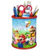 Na zdjęciu znajduje się przybornik w kształcie walca, złożony z puzzli 3D, przedstawiający postacie z gry Super Mario, takie jak Mario, Luigi, Peach i inne. W przyborniku umieszczone są różne przybory, takie jak nożyczki, pędzle, kredki i długopisy.