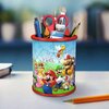 Na zdjęciu znajduje się przybornik w kształcie walca, złożony z puzzli, z motywem postaci z gry Super Mario. W przyborniku umieszczone są różne przybory biurowe, takie jak nożyczki, pędzle, ołówki i kredki.