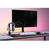 Na zdjęciu znajduje się biurko z monitorem, klawiaturą z podświetleniem RGB, myszką oraz stojakiem na słuchawki, na którym umieszczone są białe słuchawki. Tło monitora jest czarne z wzorem złożonym z małych trójkątów.