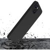 Czarne etui na telefon unosi się nad powierzchnią, z której unoszą się fragmenty gruzu, sugerując uderzenie. Tło jest białe, a etui ma wycięcia na aparat i przyciski.