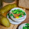 Na zdjęciu widoczne są zakrętki z kolorowym nadrukiem przedstawiającym ogórki, liście i drewnianą skrzynkę, a także napis "because homemade is better!" oraz adres strony "www.browin.com". Obok zakrętek znajdują się plasterki ogórków kiszonych i kromka chl