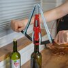 Na zdjęciu widoczny jest ręczny korkociąg z czerwonym mechanizmem, używany do zamykania butelki z ciemnego szkła. Obok stoi inna butelka z etykietą przedstawiającą kiść winogron.