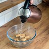 Czajnik wlewa wodę do szklanej miski, w której znajdują się korki do butelek. Miska stoi na drewnianym blacie kuchennym.