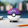 Na zdjęciu znajduje się trójwymiarowa kula złożona z puzzli, przedstawiająca Master Ball z serii Pokemon, z widoczną literą "M" na fioletowym tle. Kula stoi na czarnej podstawce, a obok niej leży żółty ołówek na białej powierzchni.