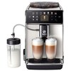 Ekspres do kawy w kolorze białym z wyświetlaczem dotykowym, na którym widoczne są ikony różnych rodzajów kaw, w tym "Espresso", "Cappuccino" i "Latte Macchiato". Obok ekspresu znajduje się pojemnik na mleko z podziałką, a pod dyszami stoją dwa szklane kub