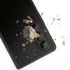 Czarny smartfon z trzema obiektywami aparatu, na które spadają kawałki skał i drobne odłamki. Obiektywy są chronione przez nakładkę, a tło jest białe.