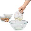 Na zdjęciu widoczna jest ręka trzymająca miarkę skośną OXO Good Grips 250 ml, z której wlewany jest płyn do szklanej miski. W tle znajdują się dwie miski z mąką i brązowym cukrem oraz dwa jajka, jedno z nich rozbite.