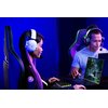 Na zdjęciu widać dwie osoby siedzące przy biurkach z laptopami, obie mają na głowach białe słuchawki z logo Razer. Na ekranie jednego z laptopów wyświetlana jest gra komputerowa.
