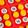 Czerwone plansze z białymi okrągłymi polami, na których znajdują się czarne liczby, są pokryte żółtymi żetonami z wytłoczonymi numerami. Widoczne liczby to m.in. 26, 35, 36, 45, 47, 48, 55, 56, 57.