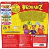 Czerwone pudełko gry karcianej "Hedbanz" z kolorowym logo na górze, przedstawia ilustracje opasek z różnymi obrazkami oraz trójkę dzieci z opaskami na głowach. Na dole znajdują się ostrzeżenia, informacje o producencie oraz adres strony internetowej www.s