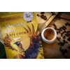 Na zdjęciu znajduje się żółte opakowanie kawy ziarnistej z napisem "Morning Bird CAFE CREMA" oraz grafiką ptaka z rozpostartymi skrzydłami. Obok opakowania stoi filiżanka z kawą, a wokół rozsypane są ziarna kawy.