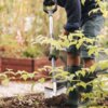 Osoba pracuje w ogrodzie, używając szpadla prostego marki FISKARS Ergonomic 1067512, w otoczeniu roślin i podniesionych grządek. Widoczne są zielone kalosze z napisem "VIKING".