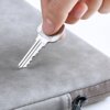 Na zdjęciu widoczne jest szare etui na laptopa, na które ktoś przykłada metalowy klucz. Etui ma gładką powierzchnię i widoczny jest zamek błyskawiczny.
