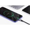 Na zdjęciu widać smartfon z wyświetlaczem pokazującym ikonę ładowania z napisem "100%", podłączony do kabla USB-C z widocznym logo "UGREEN". W tle znajdują się fragmenty dwóch innych urządzeń elektronicznych.