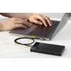 Na zdjęciu widoczny jest laptop, do którego podłączony jest czarny kabel kątowy USB-C - USB-C, łączący się z czarnym urządzeniem z logo "UGREEN". Na urządzeniu znajduje się napis "Protect What You Care".