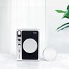Aparat fotograficzny z czarnym korpusem i srebrnymi elementami, z widocznym napisem "instax mini Evo" oraz "Fujifilm", stoi na marmurowej powierzchni obok srebrnego dekielka. W tle znajduje się fragment zielonej rośliny na jasnym tle.