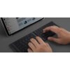 Na zdjęciu widoczna jest klawiatura złożona na pół, na której ktoś pisze, a w tle znajduje się tablet z otwartą stroną internetową. Na ekranie tabletu widoczne są nagłówki artykułów i miniatury zdjęć.