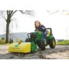 Na zdjęciu znajduje się zielono-żółty pojazd zabawkowy z logo "John Deere" na przodzie, stojący na brukowanej powierzchni w otoczeniu drzew i trawy. Pojazd ma duże czarne koła i jest wyposażony w kierownicę.
