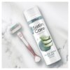 Na zdjęciu znajduje się biały pojemnik z napisem "Satin Care Sensitive Aloe Vera Glide Shave Gel 200 ml" oraz maszynka do golenia z wymienną głowicą. Tło jest marmurowe, a na opakowaniu żelu widoczne są grafiki przedstawiające aloes.