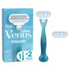 Na zdjęciu znajduje się niebieska golarka z białymi elementami oraz dwa wymienne wkłady, obok opakowania z napisem "Gillette Venus Smooth" i "Skin Cushion™". Na opakowaniu widnieje także symbol "1 + 2" przedstawiający golarkę i dwa wkłady.
