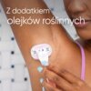 Na zdjęciu widoczna jest osoba używająca różowej golarki na wilgotnej skórze pod pachą, a w tle znajduje się kafelkowana ściana. Na zdjęciu umieszczony jest tekst: "Z dodatkiem olejków roślinnych".