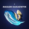 Na ciemnoniebieskim tle widoczny jest niebiesko-biały ślad kremu oraz kawałki masła kakaowego. Nad nimi znajduje się napis: "Z MASŁEM KAKAOWYM".