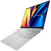Na zdjęciu widoczny jest laptop z otwartym ekranem, na którym wyświetlany jest kolorowy motyw z napisem "ASUS VivoBook" oraz oznaczeniem "OLED". Klawiatura jest jasna, a obudowa ma kilka portów po boku.
