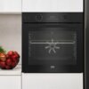 Czarny piekarnik elektryczny z panelem sterowania, na którym widoczny jest wyświetlacz z liczbą "00:34" oraz różne ikony funkcji. Na drzwiach piekarnika znajduje się logo "beko", a obok stoi misa z czerwonymi jabłkami.