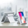 Na zdjęciu widoczne są dwie białe podstawki do urządzeń mobilnych, na jednej z nich umieszczony jest tablet, a na drugiej smartfon z wyświetlaczem pokazującym godzinę 9:41 i datę "Tuesday, September 12". Na podstawce pod smartfonem znajduje się logo "UGRE