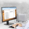 Na zdjęciu znajduje się monitor z wyświetlonym dokumentem tekstowym oraz stojak do laptopa UGREEN LP258 Srebrny, na którym umieszczony jest zamknięty laptop. Na biurku widoczna jest klawiatura, a w tle szara ściana.