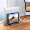 Na zdjęciu znajduje się srebrny stojak do laptopa marki UGREEN, na którym umieszczony jest laptop oraz tablet z widokiem pustyni na ekranie. Stojak stoi na drewnianym biurku, obok monitora i klawiatury, a do laptopa podłączony jest kabel.