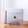 Na zdjęciu widoczny jest srebrny stojak do laptopa z logo "UGREEN", na którym umieszczone są dwa laptopy. W tle widać strzałki sugerujące przepływ powietrza wokół urządzeń.