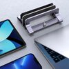 Na zdjęciu znajduje się srebrny stojak do laptopa z napisem "UGREEN", obok którego leżą otwarty laptop, tablet oraz smartfon. Stojak ma regulowaną szerokość, co umożliwia dopasowanie do różnych urządzeń.