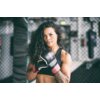 Osoba w sportowym stroju trzyma zaciśnięte pięści w rękawicach do MMA BRUTE PRO R, czarno-czerwonych, na tle siatki w sali treningowej. Na rękawicach widoczne jest logo "BRUTE".