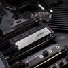 Na zdjęciu widoczny jest dysk SSD z logo "XPG" zamontowany na płycie głównej komputera. W tle widać elementy elektroniczne i złącza płyty głównej.