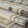 Beżowy obrus z geometrycznym wzorem w kratę oraz motywami śnieżynek i złotych linii. Materiał jest złożony, ukazując różnorodność wzorów i tekstur.