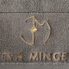 Szary ręcznik z widocznym złotym haftem przedstawiającym stylizowane logo oraz napis "EVA MINGE". Tkanina ma teksturę frotte, a haft jest umieszczony na dolnej części ręcznika.