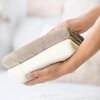 Na zdjęciu widoczne są dwie złożone ręczniki w odcieniach beżu i kremu, trzymane w dłoniach. Tło jest rozmyte, co podkreśla miękkość i fakturę ręczników.