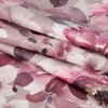 Zdjęcie przedstawia zbliżenie na materiał z wzorem kwiatowym w odcieniach różu, bieli i fioletu. Tkanina jest złożona, ukazując miękką teksturę i delikatne przejścia kolorów.