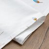 Biała serweta z delikatnym wzorem w postaci niebiesko-brązowych kwiatów, leży na drewnianej powierzchni. Materiał jest starannie złożony, ukazując teksturę tkaniny.