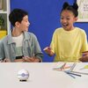 Na zdjęciu znajduje się biały stół, na którym leży zestaw kolorowych kredek, otwarty zeszyt oraz puzzle 3D w kształcie piłki uzdrawiającej z motywem Pokemon. W tle widoczna jest niebieska ściana oraz fragment białego regału z rośliną i żółtym pudełkiem.