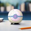 Na zdjęciu znajduje się trójwymiarowa kula z puzzli, przedstawiająca piłkę uzdrawiającą z motywem Pokemon, umieszczona na czarnym stojaku. Obok kuli leży ołówek, a w tle widać rozmyte kształty, które mogą być książkami na półce.