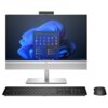 Na zdjęciu znajduje się komputer typu all-in-one z widocznym ekranem, na którym wyświetlany jest interfejs systemu Windows 11. Przed komputerem umieszczona jest klawiatura oraz myszka, a na obudowie monitora widoczne jest logo HP.