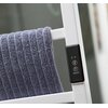 Na zdjęciu widoczny jest fragment białego grzejnika elektrycznego z szarym ręcznikiem zawieszonym na poprzeczce. Obok znajduje się panel sterujący z przyciskami oznaczonymi symbolami zegara, napisem "ON/OFF" oraz logo "InnovaGoods".