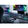 Na zdjęciu znajduje się biurko z klawiaturą, myszką i dużym monitorem, na którym widoczny jest kolorowy wzór z logo Razer. Obok monitora stoi laptop z podobnym wzorem na ekranie, a na biurku leżą słuchawki.