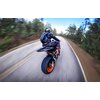 Na zdjęciu widać motocyklistę jadącego po krętej drodze otoczonej drzewami. Motocykl ma pomarańczowe felgi, a tło jest rozmyte, co sugeruje ruch.