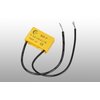 Żółty komponent elektroniczny z dwoma czarnymi przewodami, na którym widnieje tekst: "MCR-P, 0.1uF+100Ω, 1/2W, 600V AC" oraz symbole certyfikacyjne. Przewody mają oznaczenia techniczne na swojej powierzchni.