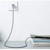 Na zdjęciu widać czarny kabel USB-A - USB-C podłączony do gniazdka ściennego, z drugiej strony podłączony do smartfona leżącego na stosie książek. Na grzbietach książek widoczne są napisy: "AD SELECT MONTHLY VOLUME 004", "Hannah Weitemeier", "YVES".
