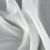 Biała firana o delikatnej, przezroczystej strukturze układa się w miękkie fałdy. Materiał jest lekki i zwiewny, co nadaje mu elegancki wygląd.